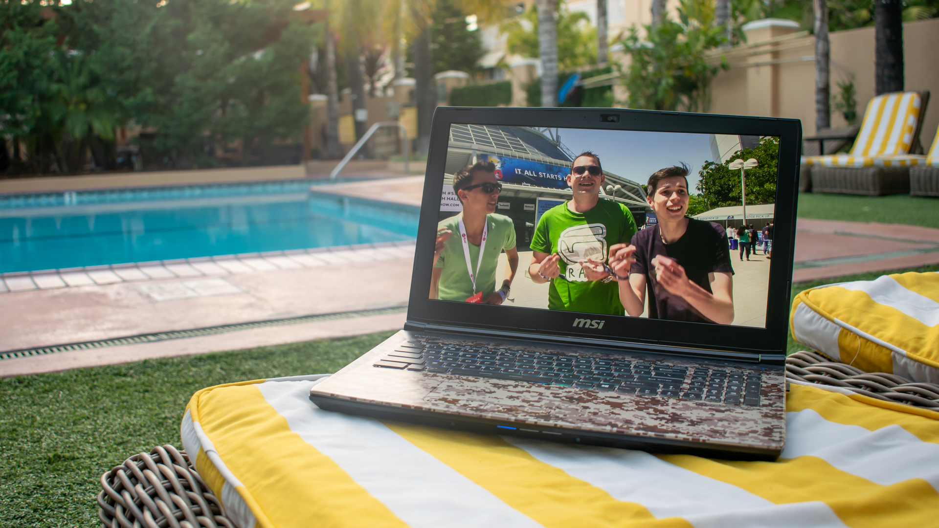Foto van een laptop bij een zwembad in Los Angeles. Op de laptop staat een video-verslag van E3 2017 aan, met presentatiebeeld van Leon, Peter en Tom